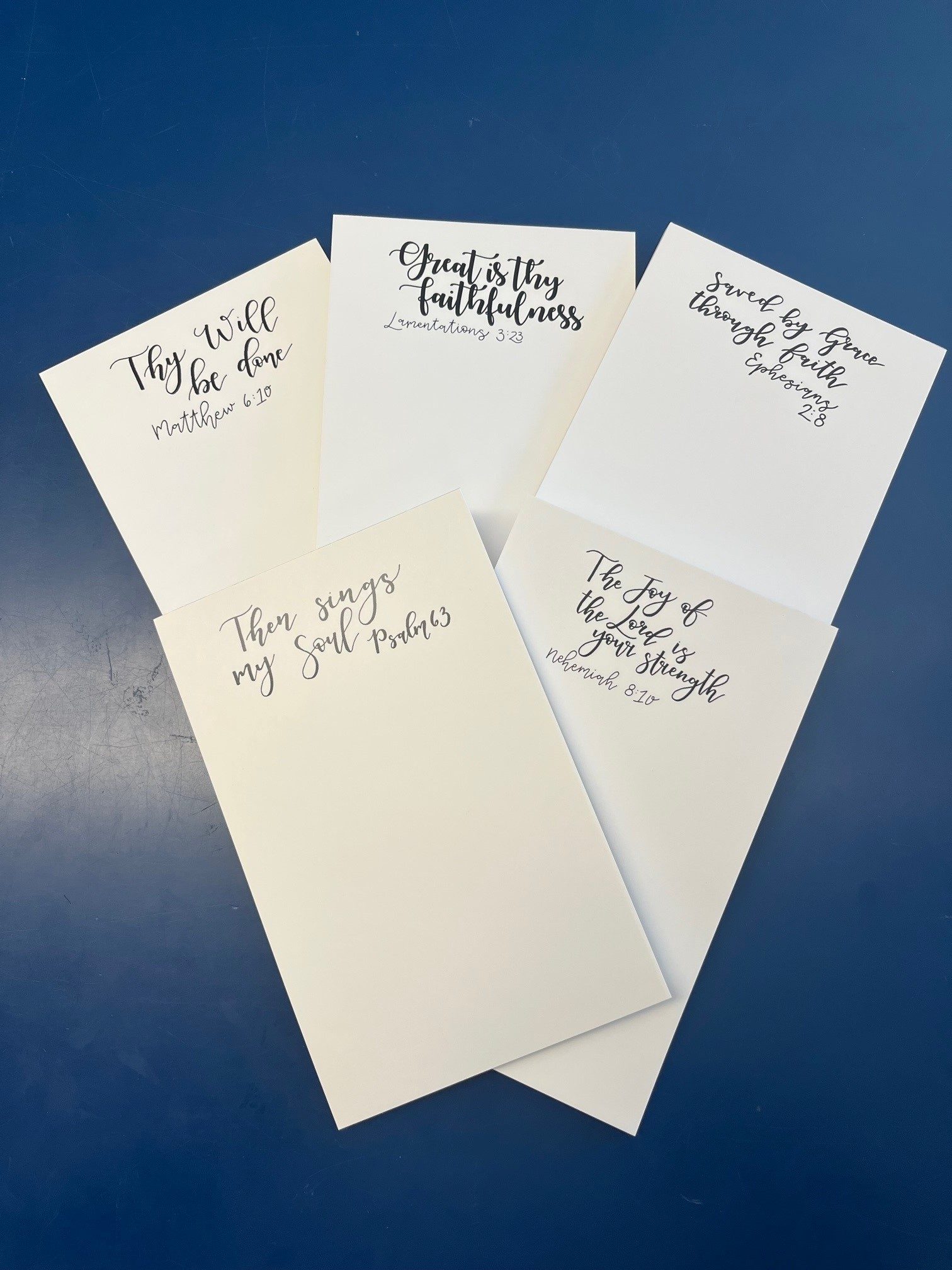 Five cream scripture notepads fanned on a blue surface.